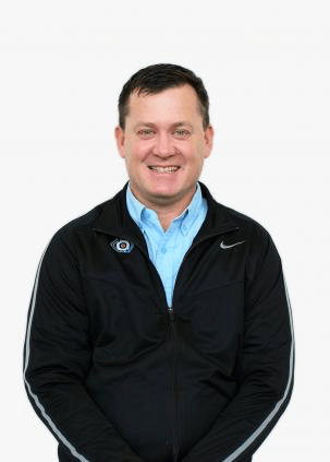 A man wearing a black nike jacket and a blue shirt is smiling.