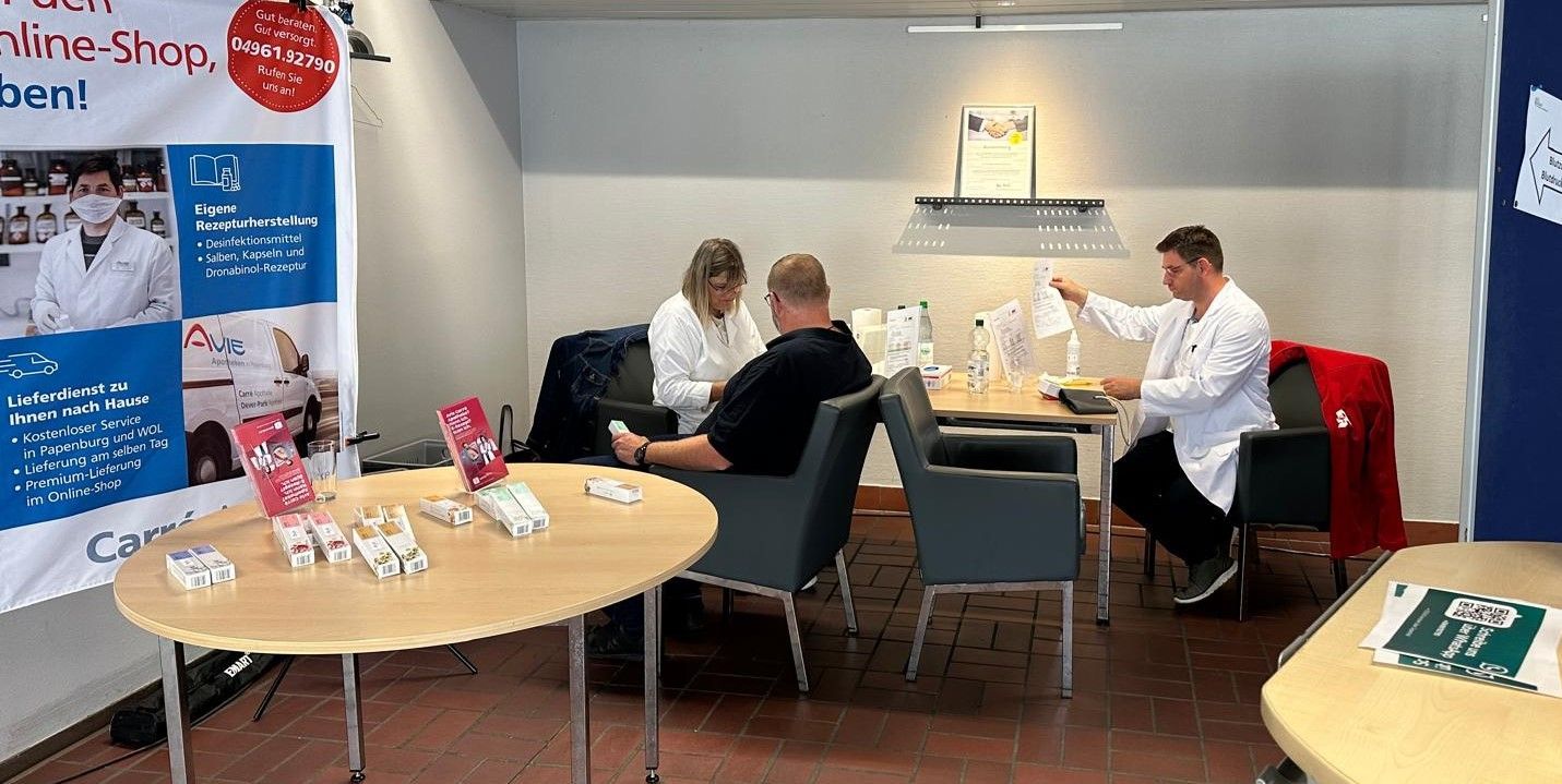 Ein Mediziner im Laborkittel bedient Kunden an einem Tisch in einem Raum.