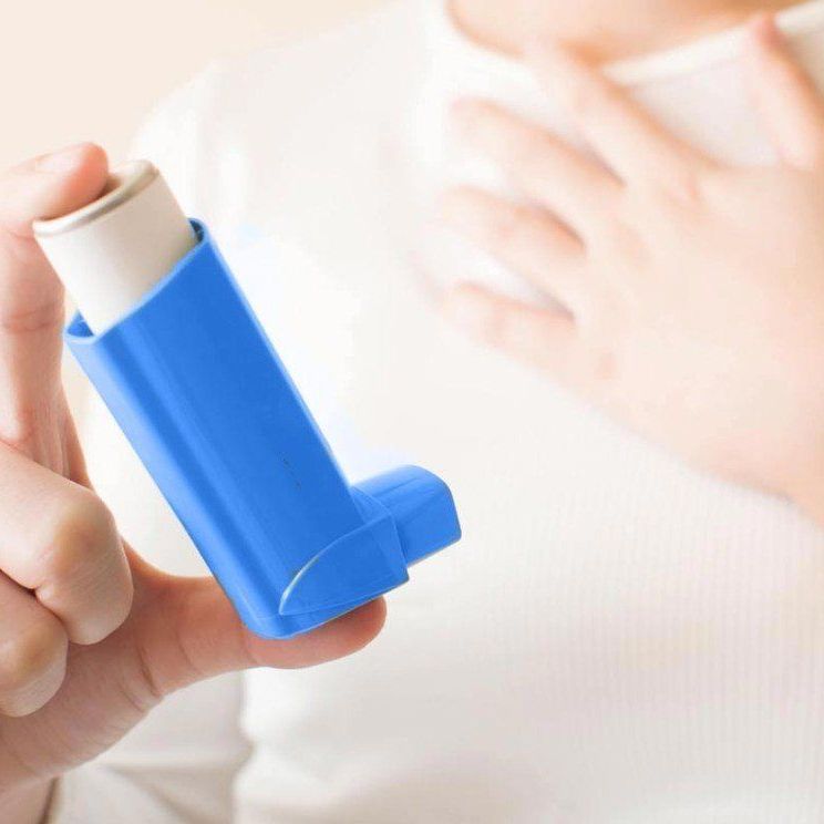 Eine Person hält einen blauen Inhalator in der Hand.
