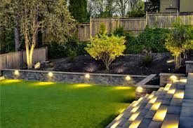 A backyard with a lush green lawn and stairs leading up to it. Project completed by Aarons lighting & Design. 