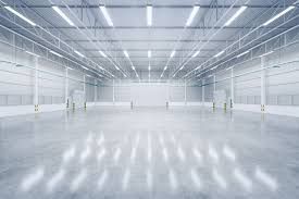 A large empty warehouse with a concrete floor and ceiling project lights completed by AARONS Lighting & Design. 