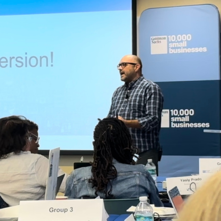 A man giving a presentation in front of a screen that says 10,000 small businesses