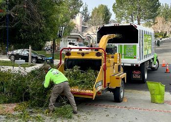 A man is working on a tree chipper in front of a truck.