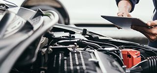 A mechanic is using a laptop computer while working on a car.