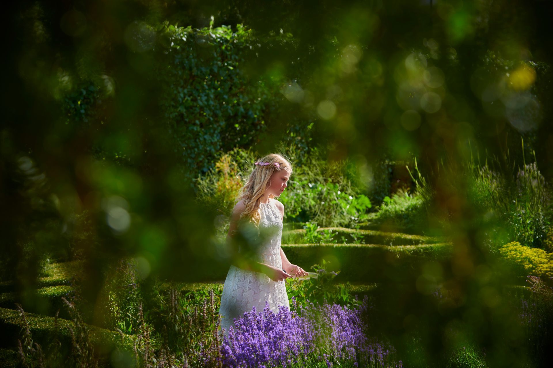 Una donna vestita di bianco è in piedi in un giardino con fiori viola.
