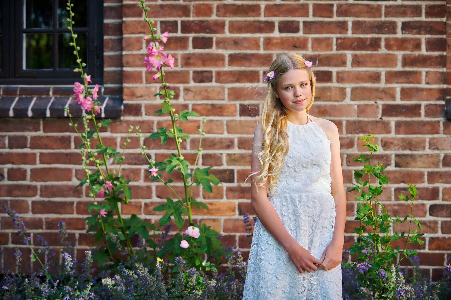 Una ragazza vestita di bianco è in piedi davanti a un muro di mattoni.