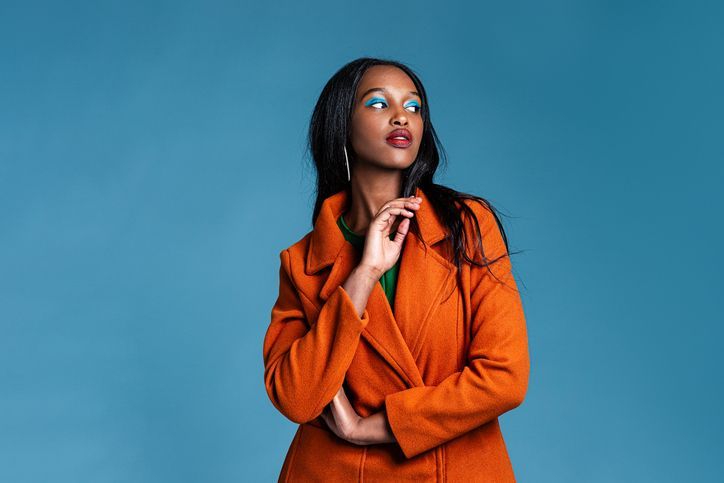 Una donna con un cappotto arancione è in piedi davanti a uno sfondo blu.