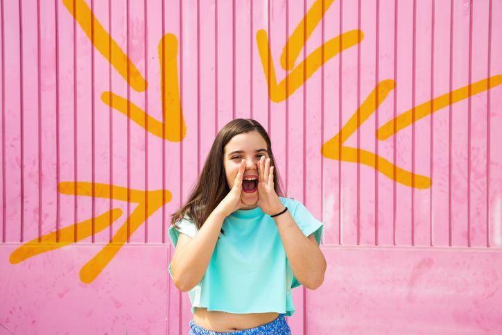 Una giovane donna sta urlando in un microfono davanti a un muro rosa.