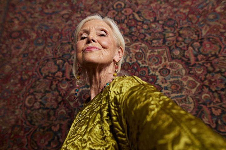 Una donna anziana con un vestito giallo si sta scattando un selfie.