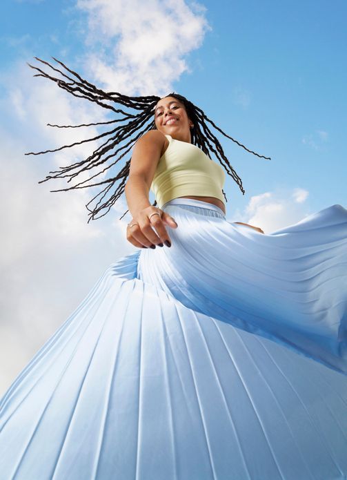 Una donna con i dreadlocks indossa una gonna plissettata azzurra.