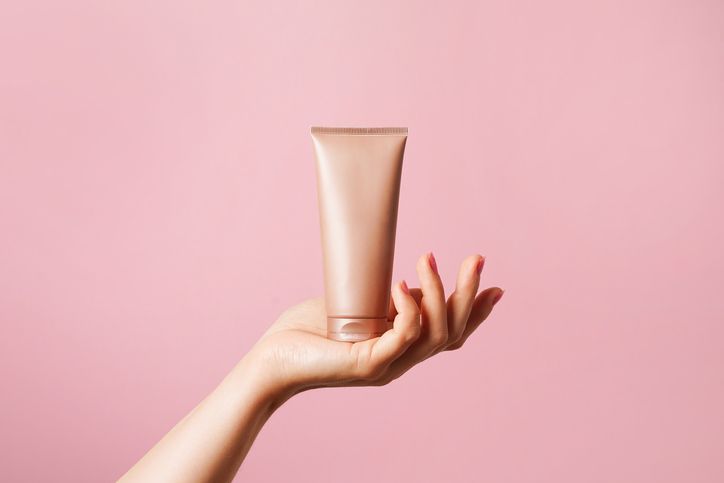 La mano di una donna tiene un tubetto di lozione su uno sfondo rosa.