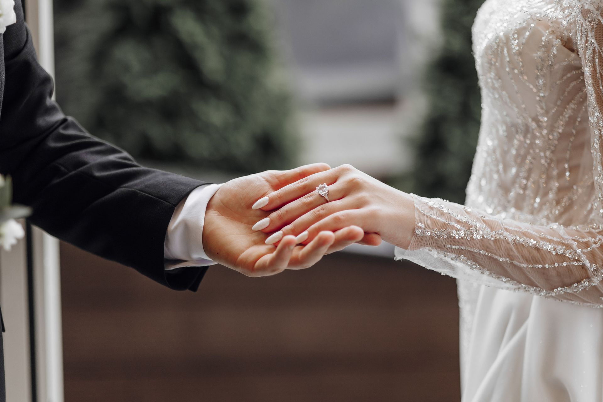 Una sposa e uno sposo si tengono per mano e la sposa indossa un anello di fidanzamento.