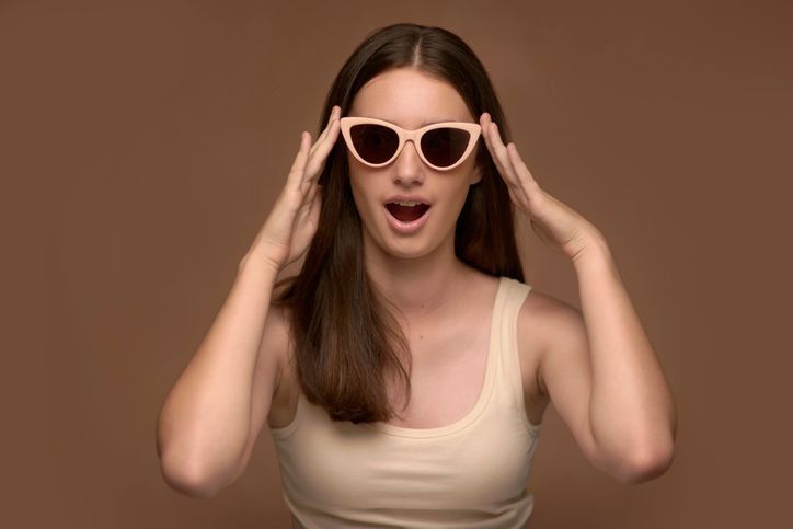 Una donna che indossa occhiali da sole e canotta fa una faccia sorpresa.