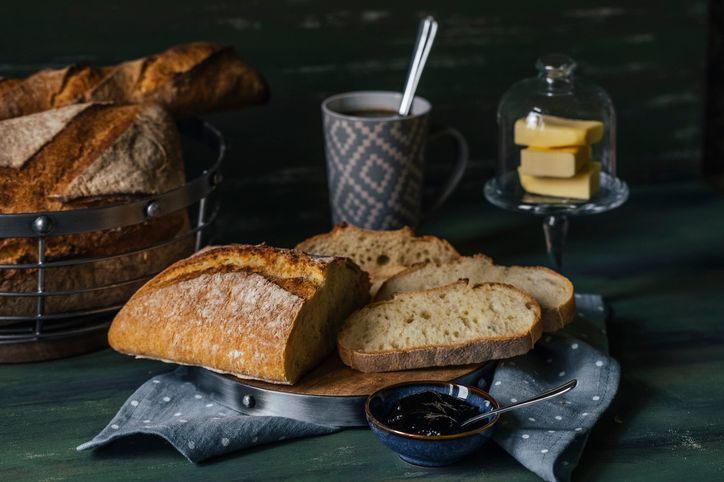 Una pagnotta di pane è appoggiata su un tavolo accanto a una tazza di caffè e burro.