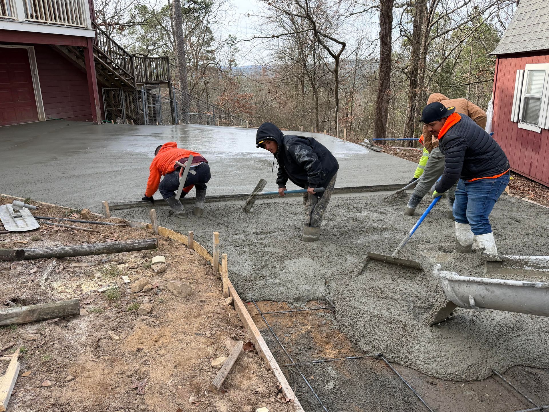 Two workers spreading dark aggregate concrete in wooden forms at a construction site.