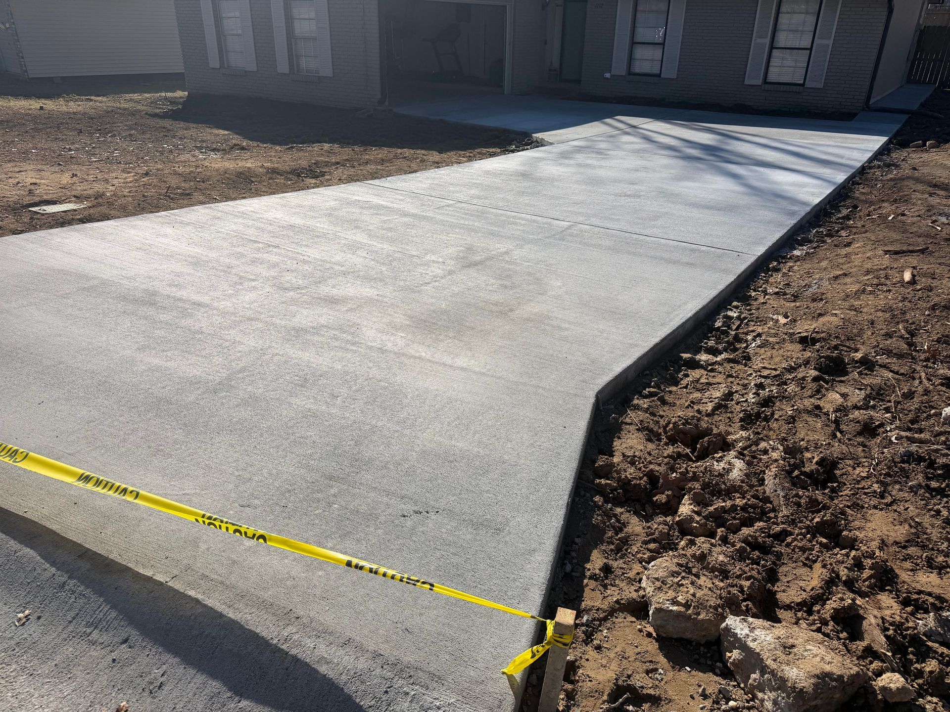 Beige two-story house with a brown garage door, driveway, and shutters. Blue sky and green grass.