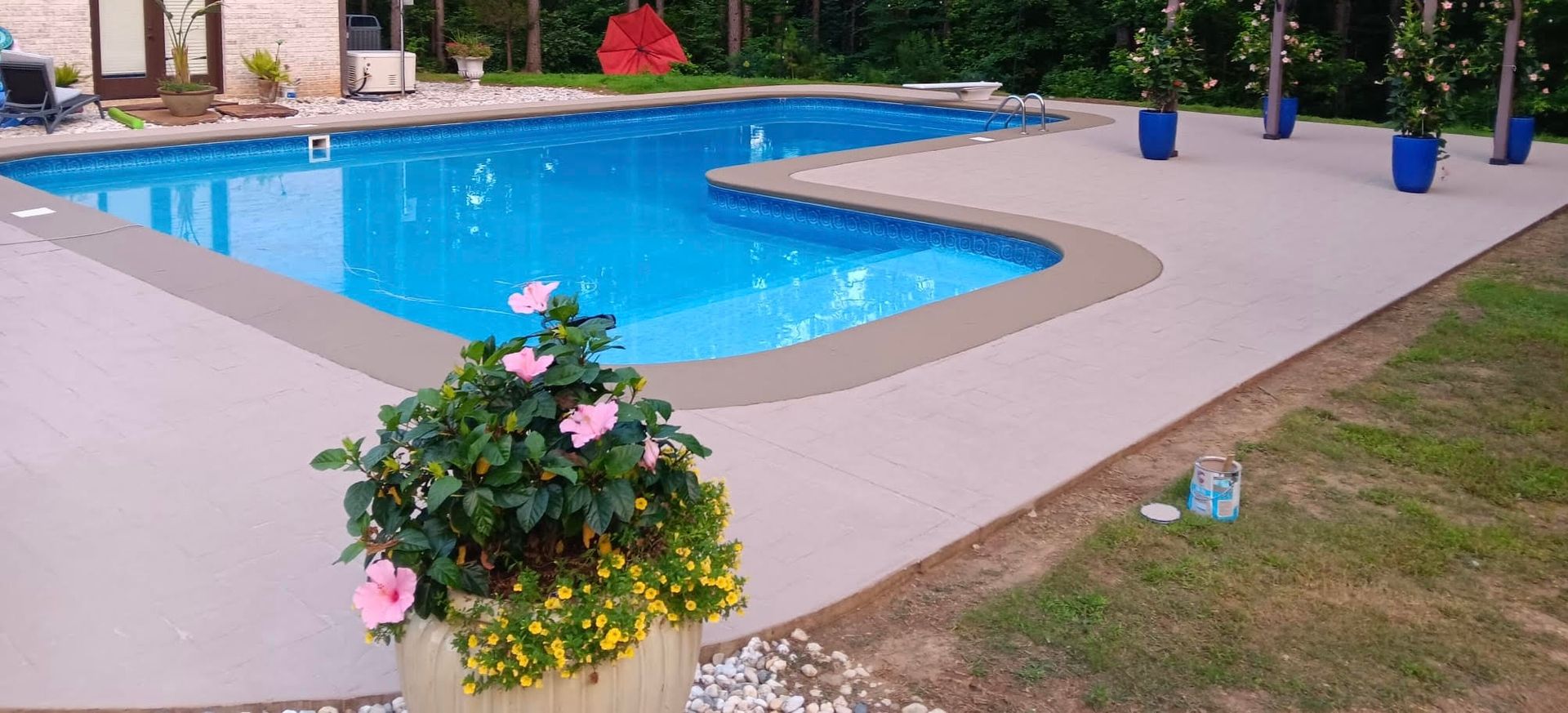 Backyard with a pool, spa, patio, and white house. Landscaped with trees and flowers.