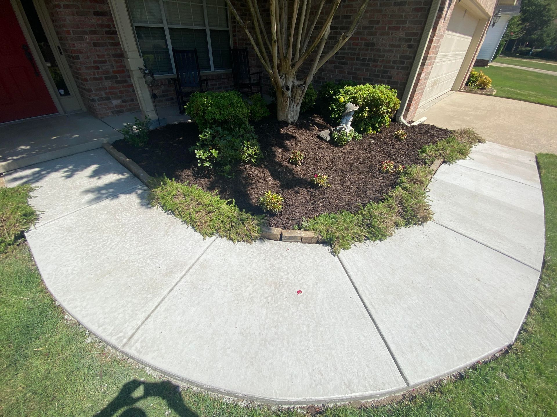 Sidewalk flanked by green grass and bollards, leading to a residential street.