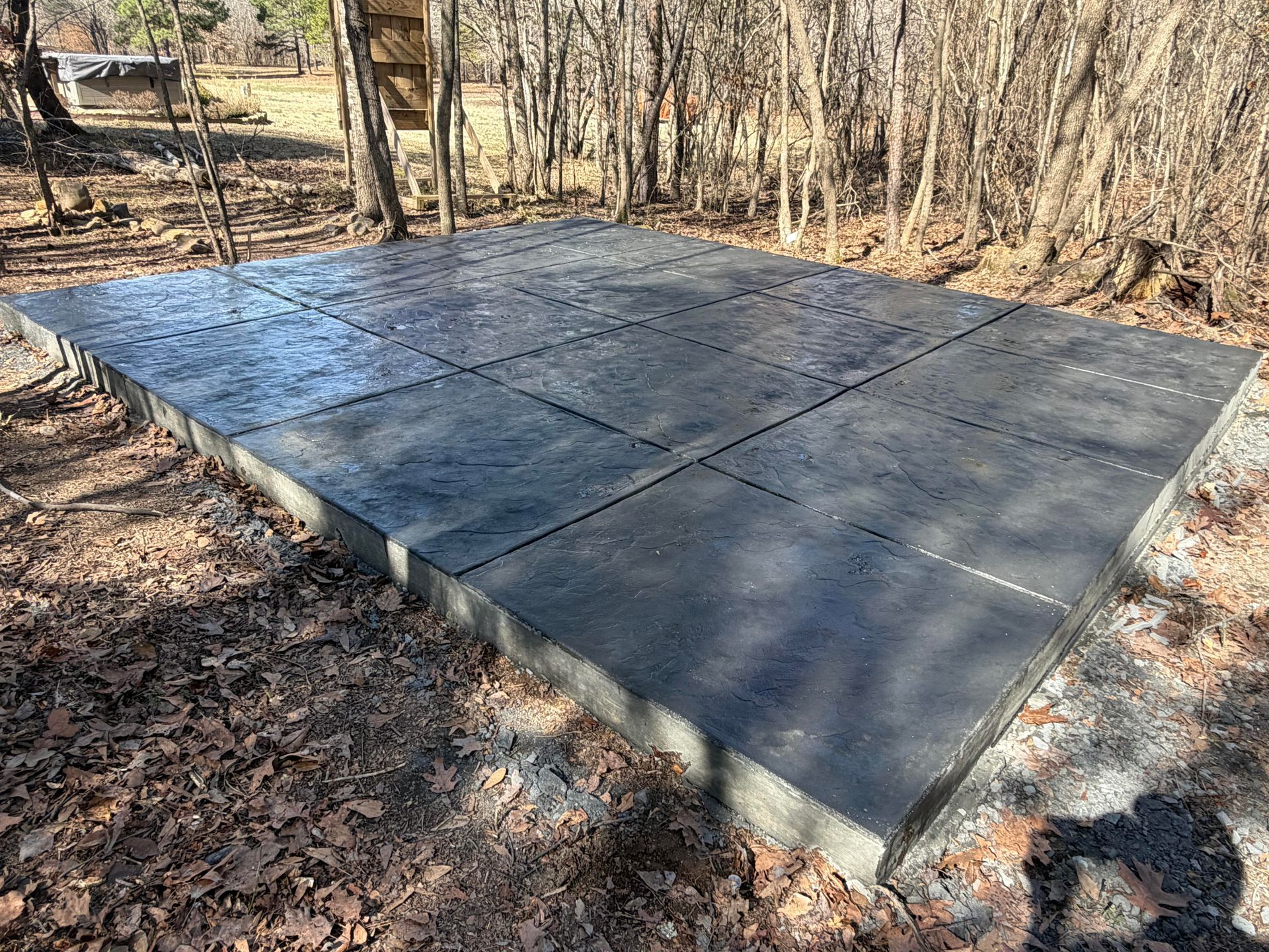 Stamped concrete patio with a curved edge, adjacent to a wooden deck, set outdoors on a sunny day.