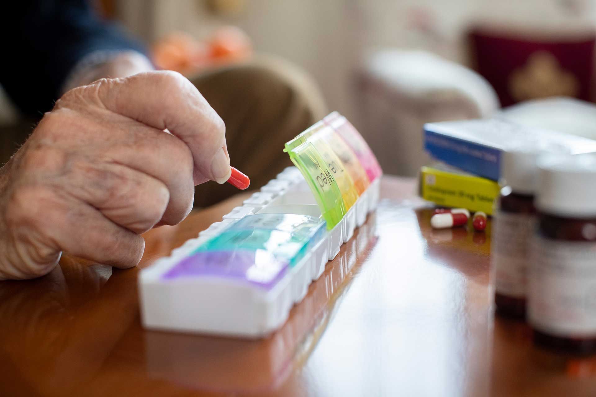 An elderly man is taking a pill from a pill box.