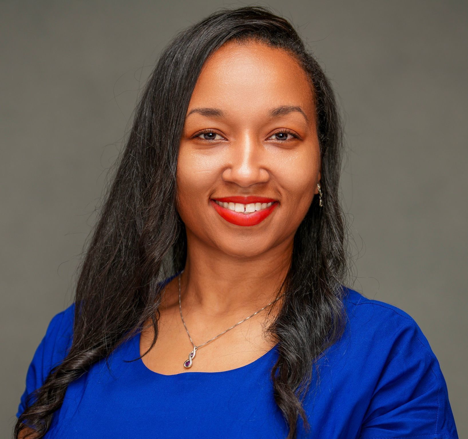 A woman in a blue dress and red lipstick is smiling for the camera. Tayese S. Greenaway