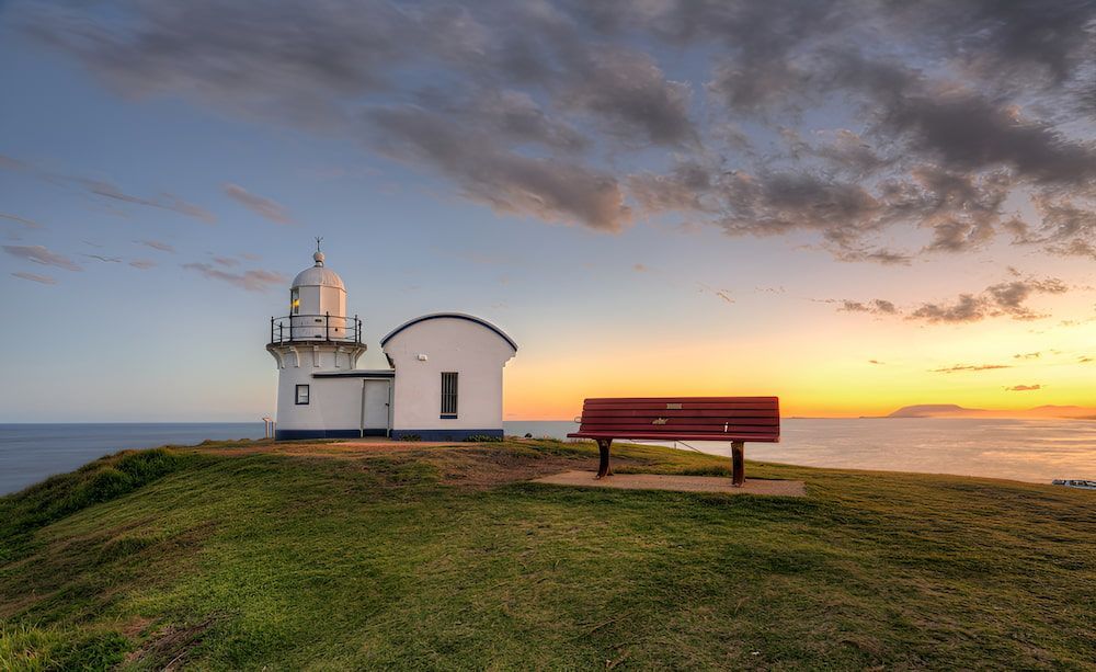 A Lighthouse And A Bench On A Cliff Overlooking The Ocean At Sunset — Alex's Vegetation in Port Macquarie, NSW