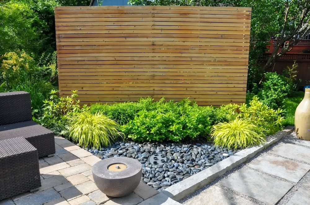 A Patio With A Wooden Fence Surrounded By Plants And Rocks — Alex's Vegetation in Port Macquarie, NSW