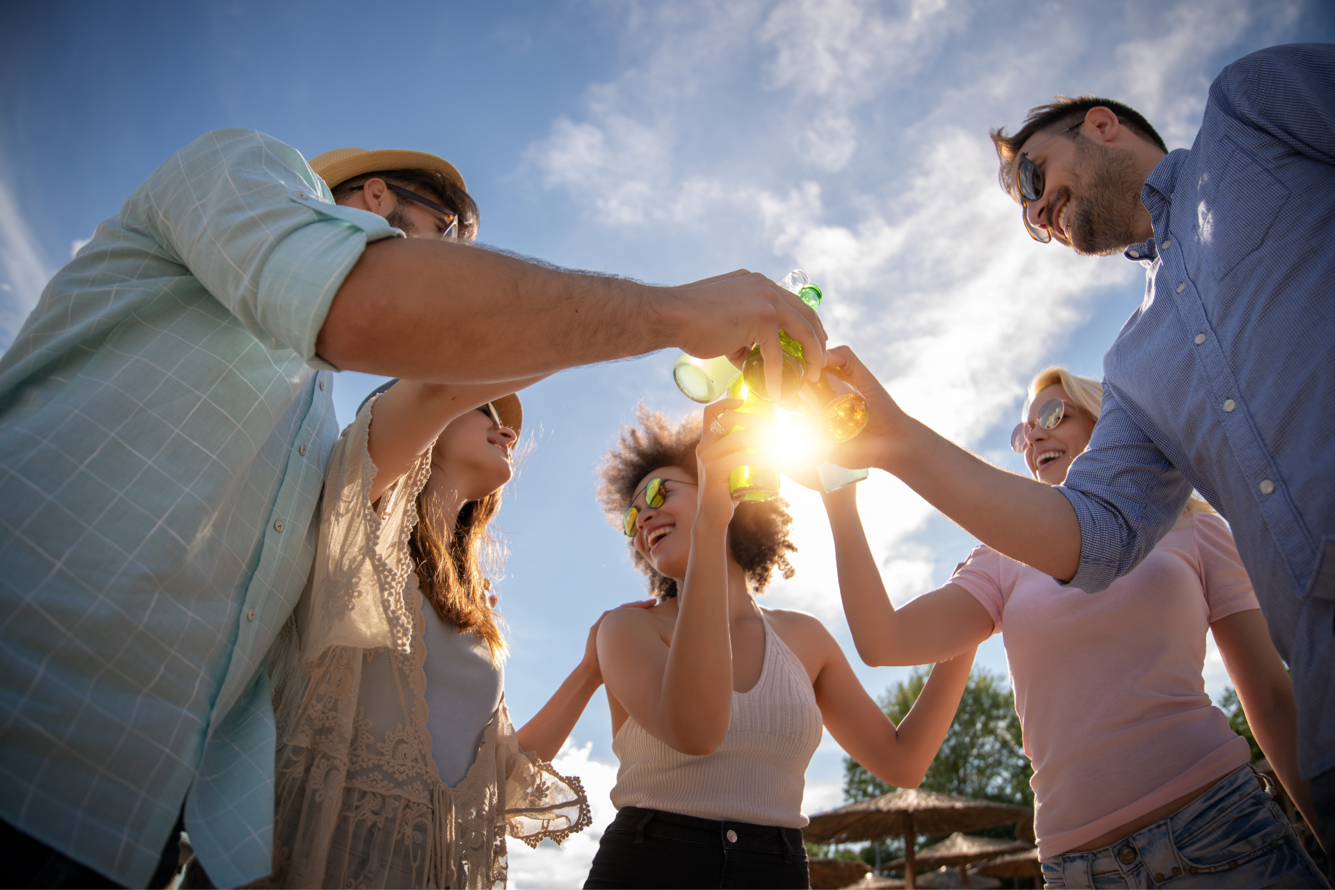 A group of people are toasting with beer bottles in front of the sun.