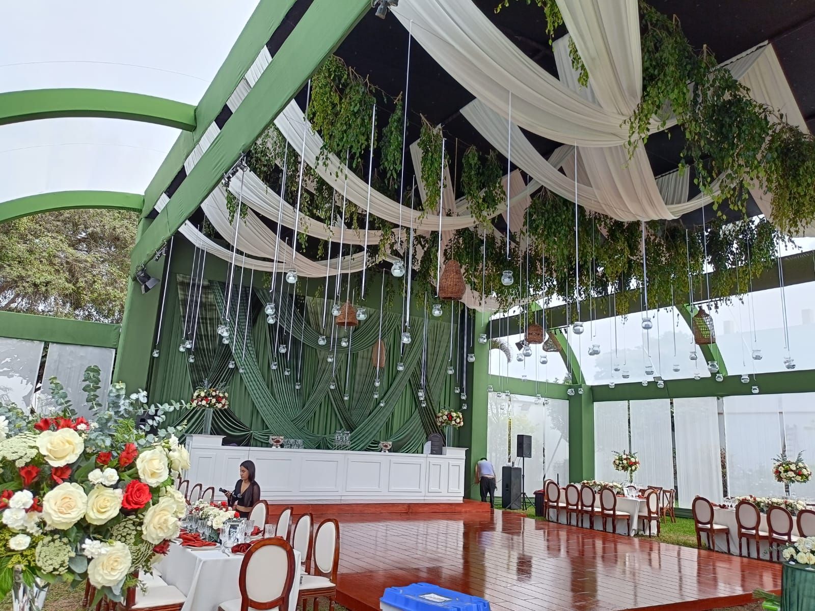 Elegante salón de eventos en verde y blanco con techo decorado con cortinas, centros de mesa florales y sillas de madera