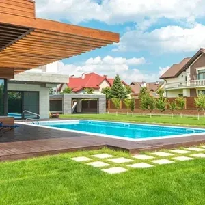 Modern backyard with blue swimming pool, green lawn, and contemporary houses under a partly cloudy sky