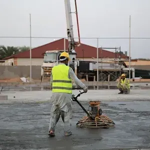 Worker in neon vest smoothing wet concrete on a construction site with a power trowel.