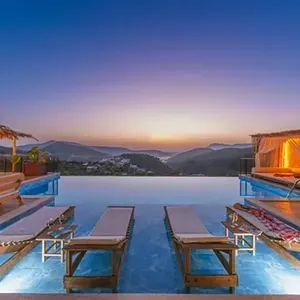 Infinity pool at sunset with two lounge chairs, mountain view, and warm-lit cabanas