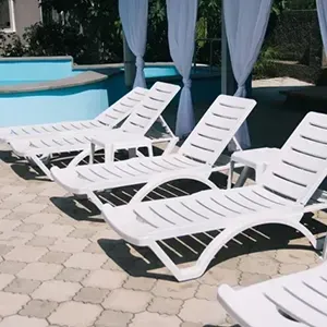 White lounge chairs beside a pool on a sunny patio with draped cabanas.