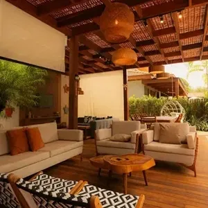 Open-air patio with beige sofas, wooden table, hanging lanterns, and tropical greenery at sunset