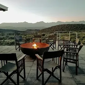 Outdoor patio with chairs around a fire pit, overlooking mountains at sunset
