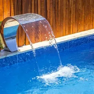 Stainless steel pool waterfall spilling into a blue swimming pool beside a wooden fence
