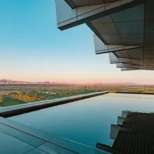 Modern pool beside a glass-walled terrace, reflecting a desert sunset and distant mountains.