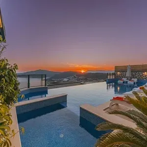 Infinity pool at sunset overlooking the sea, with lounge chairs and palm fronds on the deck.