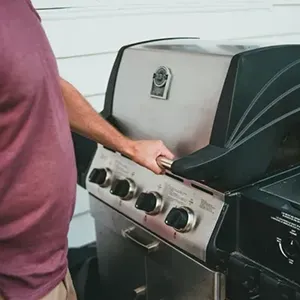 Person opening the lid of a stainless steel gas grill with black side shelf.