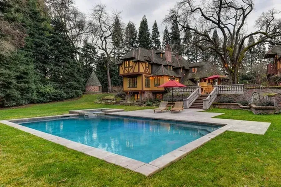 Backyard pool beside a Tudor-style house, with lounge chairs and bare trees in a landscaped yard