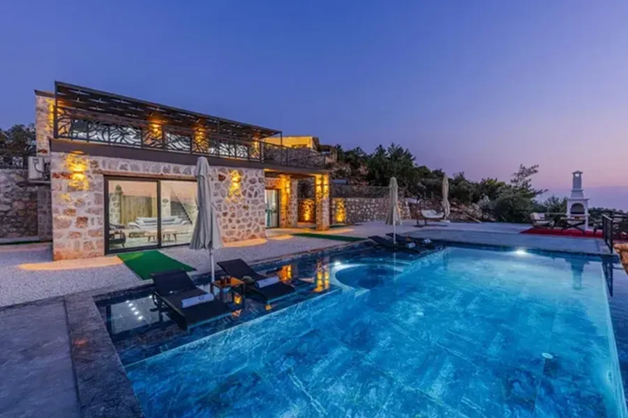 Luxury stone villa with lit pool and ocean view at dusk