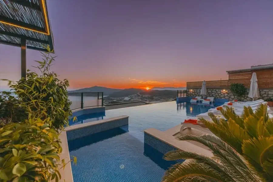Sunset over an infinity pool with lounge chairs and tropical plants on a terrace