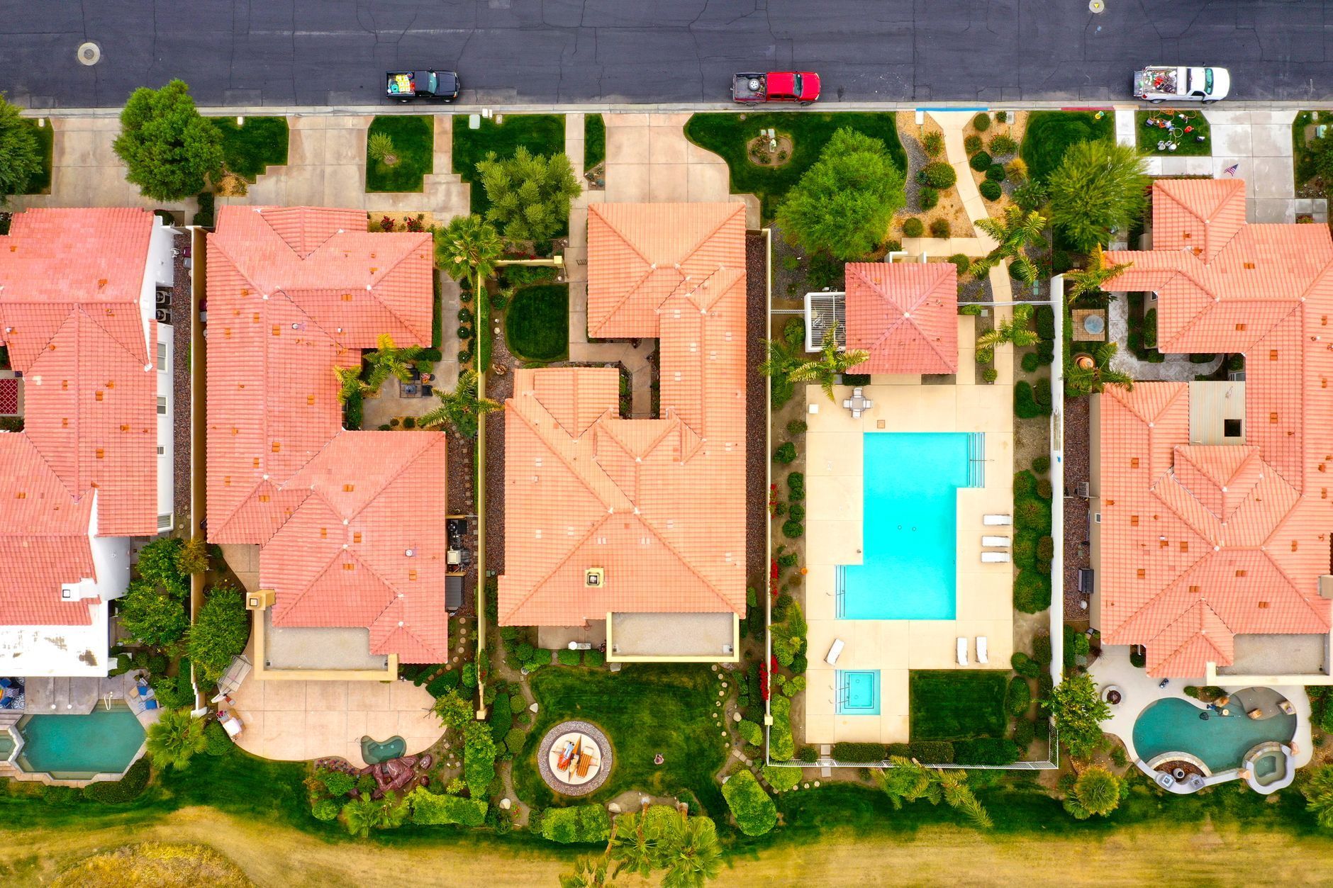 Aerial view of four seaside homes with red roofs, a central pool, and parked cars along the street.