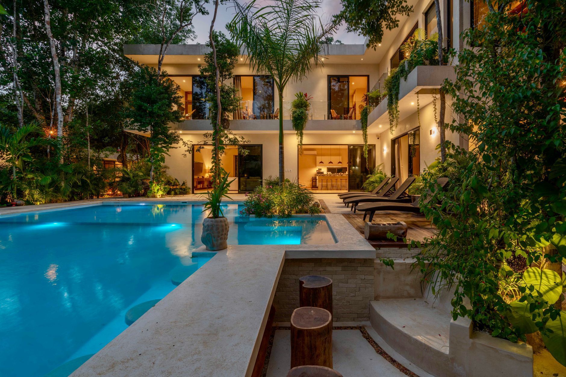Luxury resort courtyard with glowing pool, lush greenery, and lit balconies at dusk