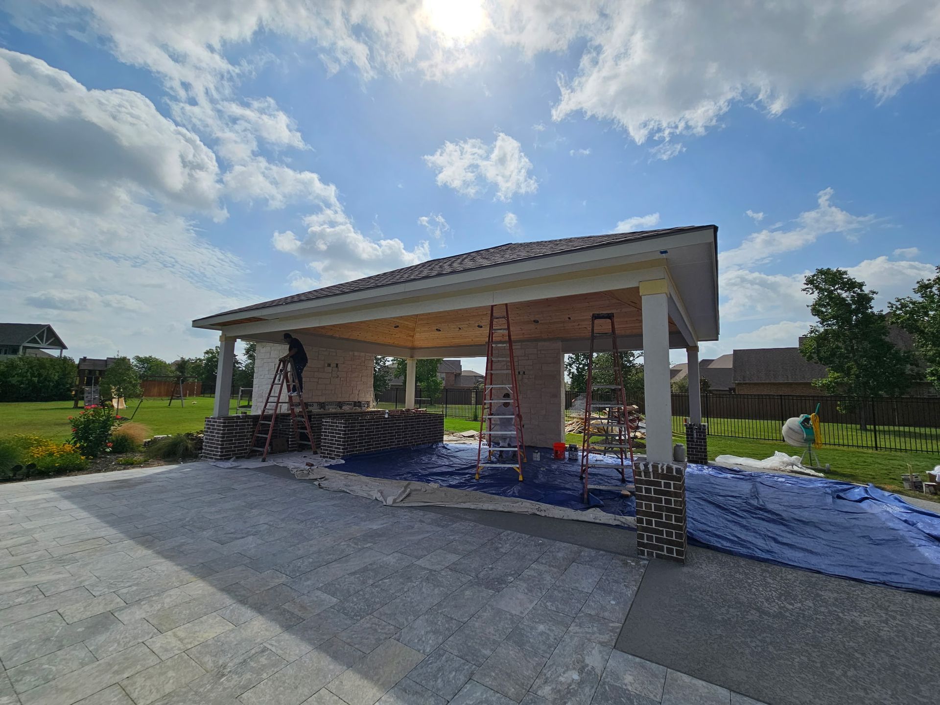 Construction site for a small pavilion with a sloped roof and stone columns under a sunny sky