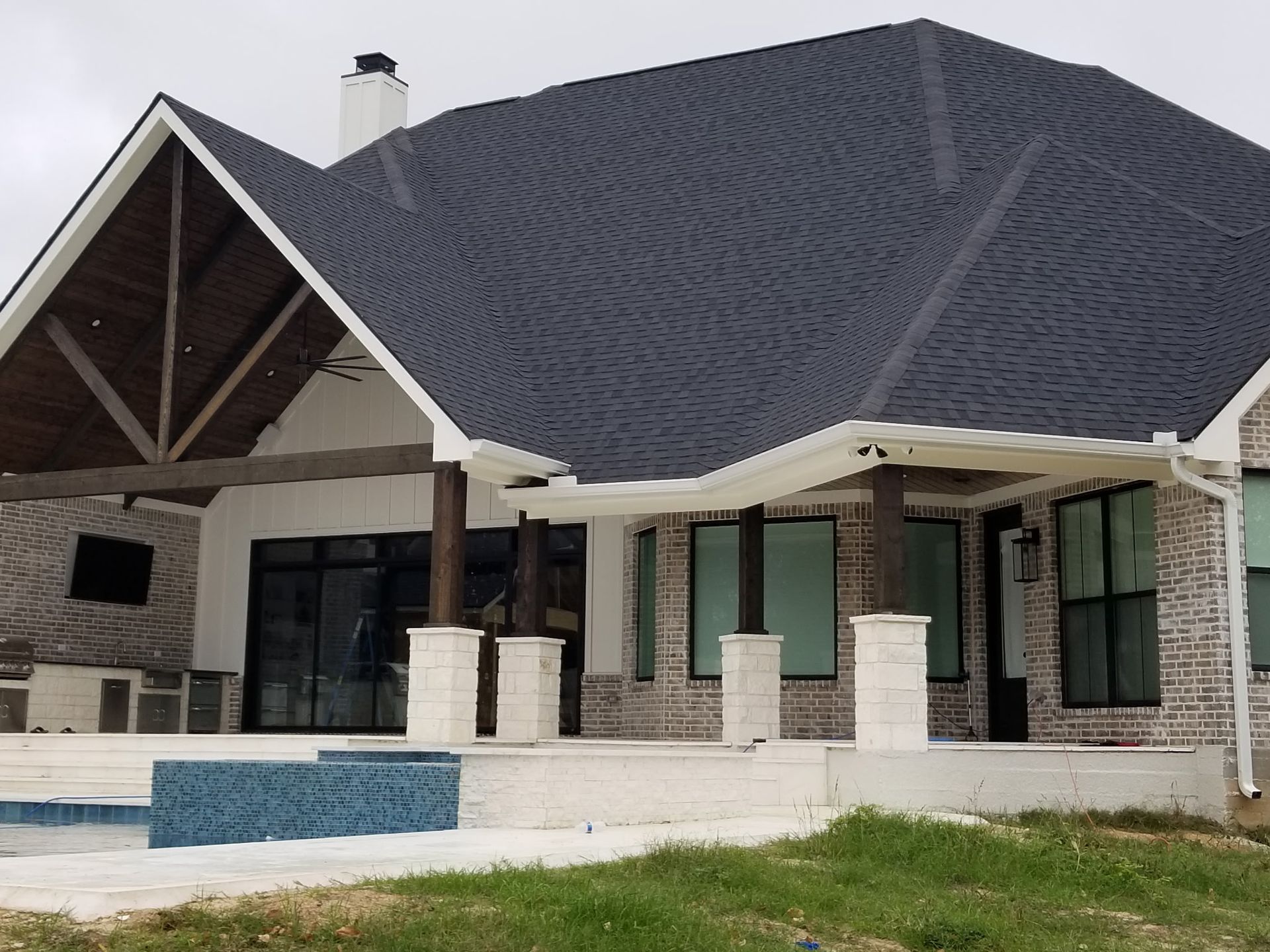 Large modern house with a dark shingled roof, stone exterior, and a small front pool