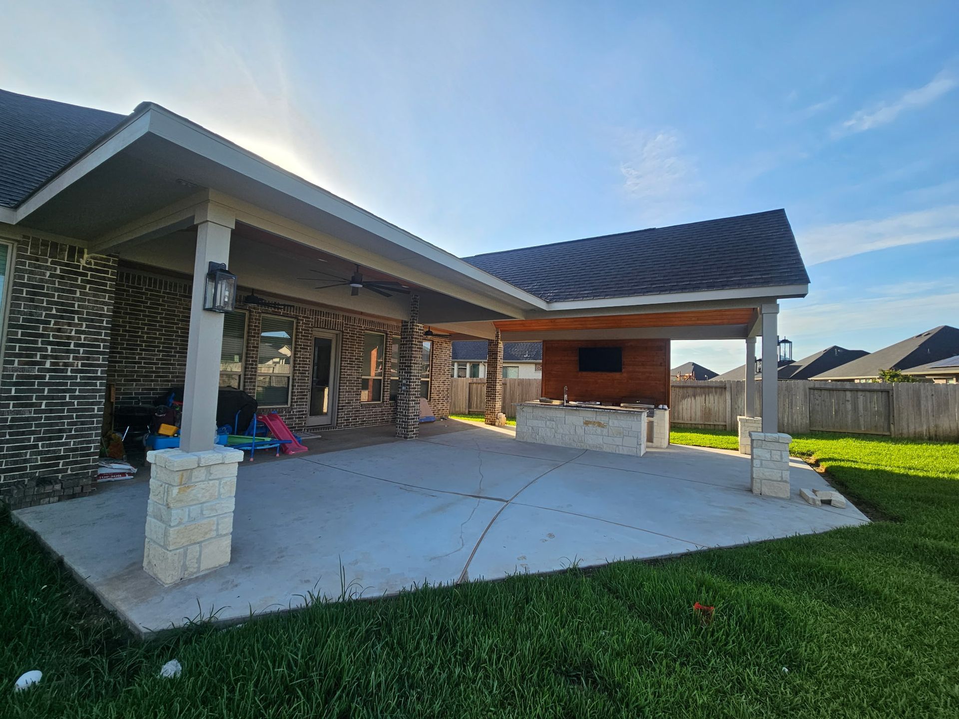 Modern house patio with stone columns, covered porch, concrete slab, and green lawn at sunset