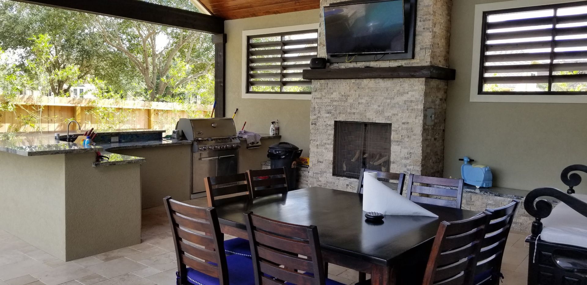 Covered patio dining area with a fireplace, TV, bar counter, and table with chairs