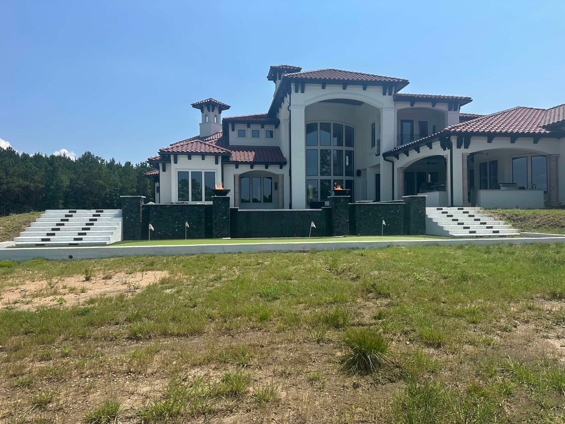 Large white Mediterranean-style mansion with red-tile roofs and a grassy foreground under a blue sky