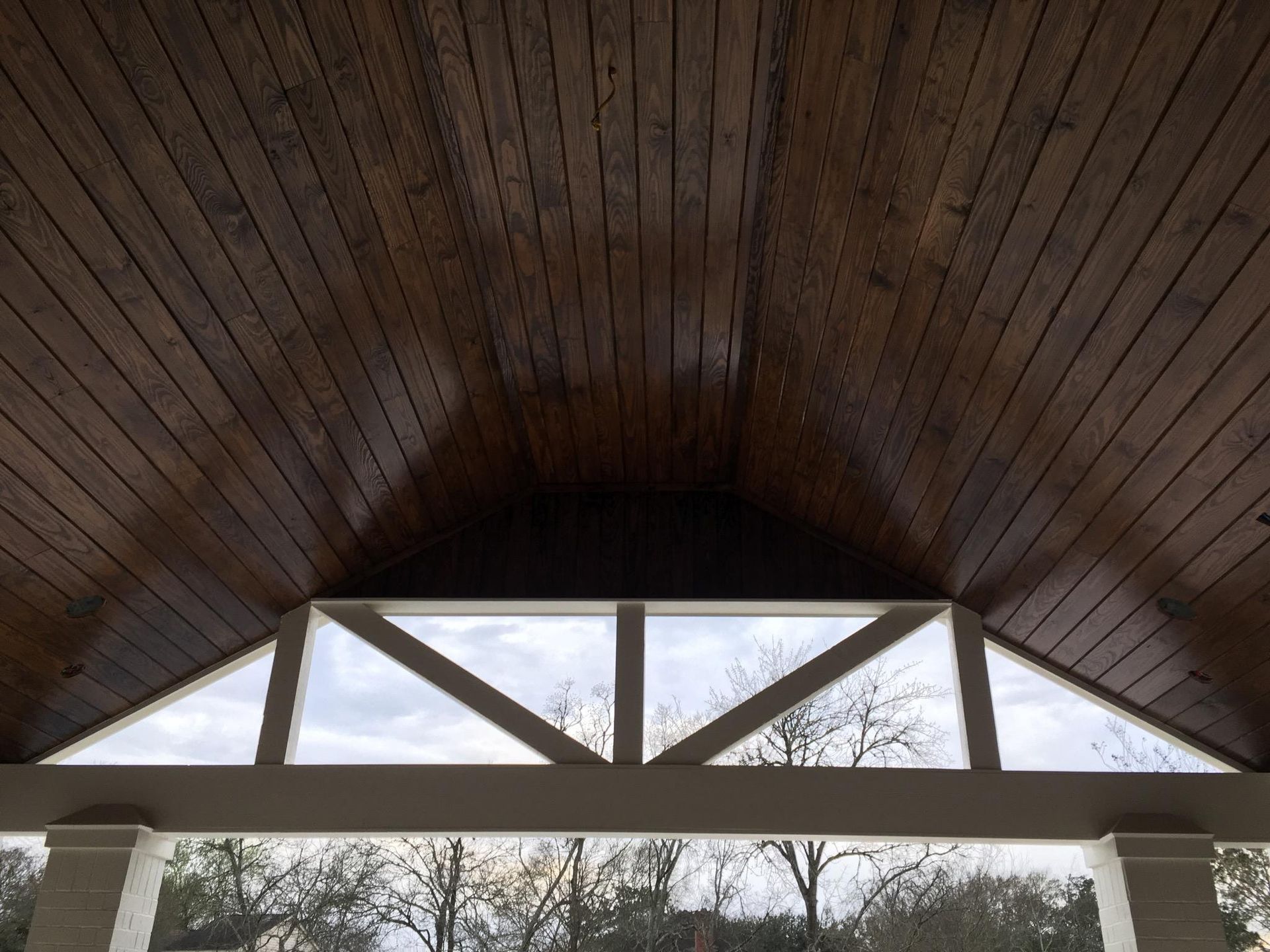 Wooden vaulted ceiling with triangular windows and trees visible outside